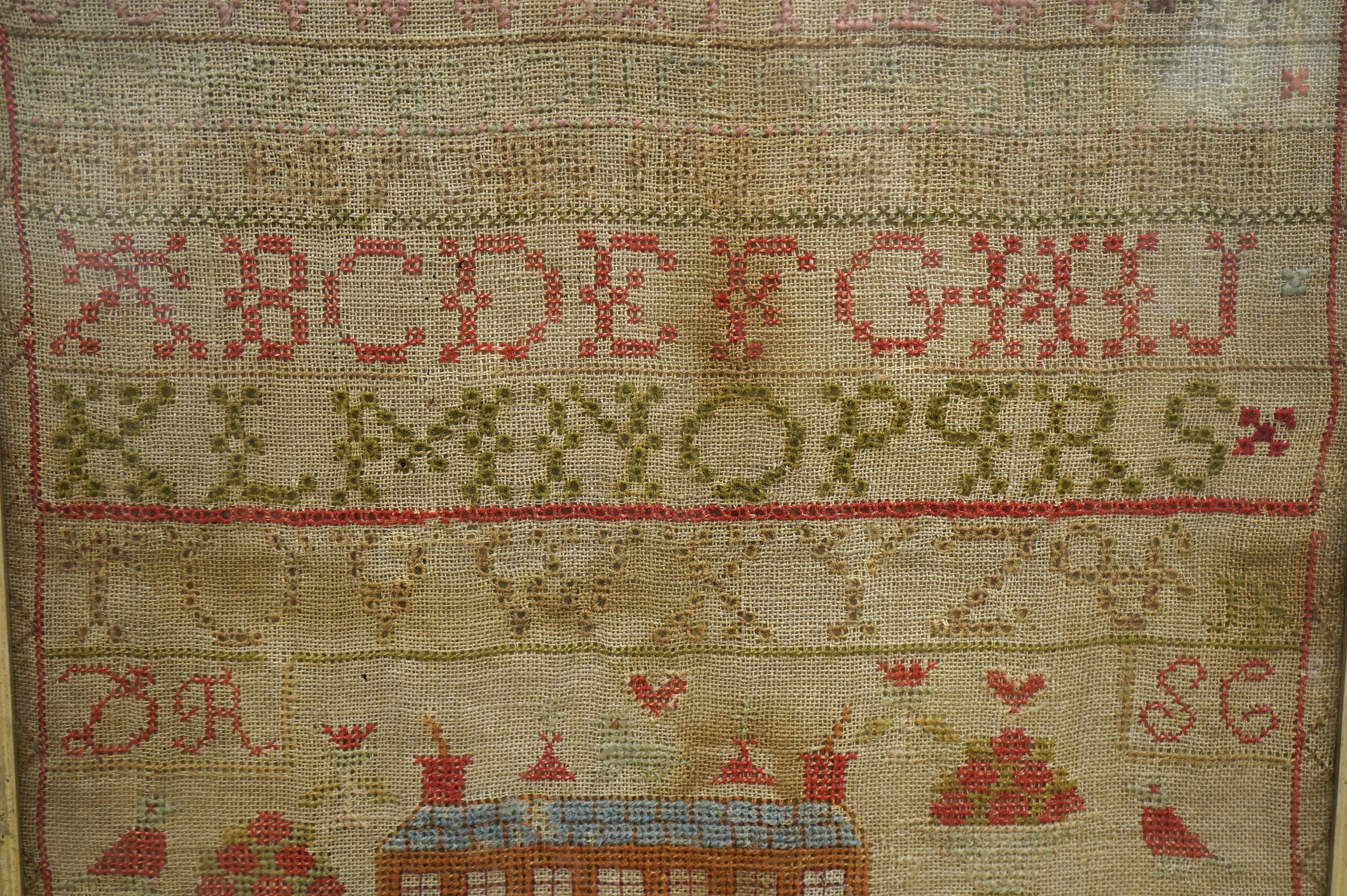 A 19th century sampler by Marion Ronald dated 1846, worked with various alphabets in cross stitch and buttonhole stitch, the lower section depicting a large thirteen windowed house surrounded by various spot motifs, a do